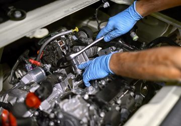 Hands of a mechanic wearing blue gloves working on a car engine with a spanner in a concept of maintenance and repair